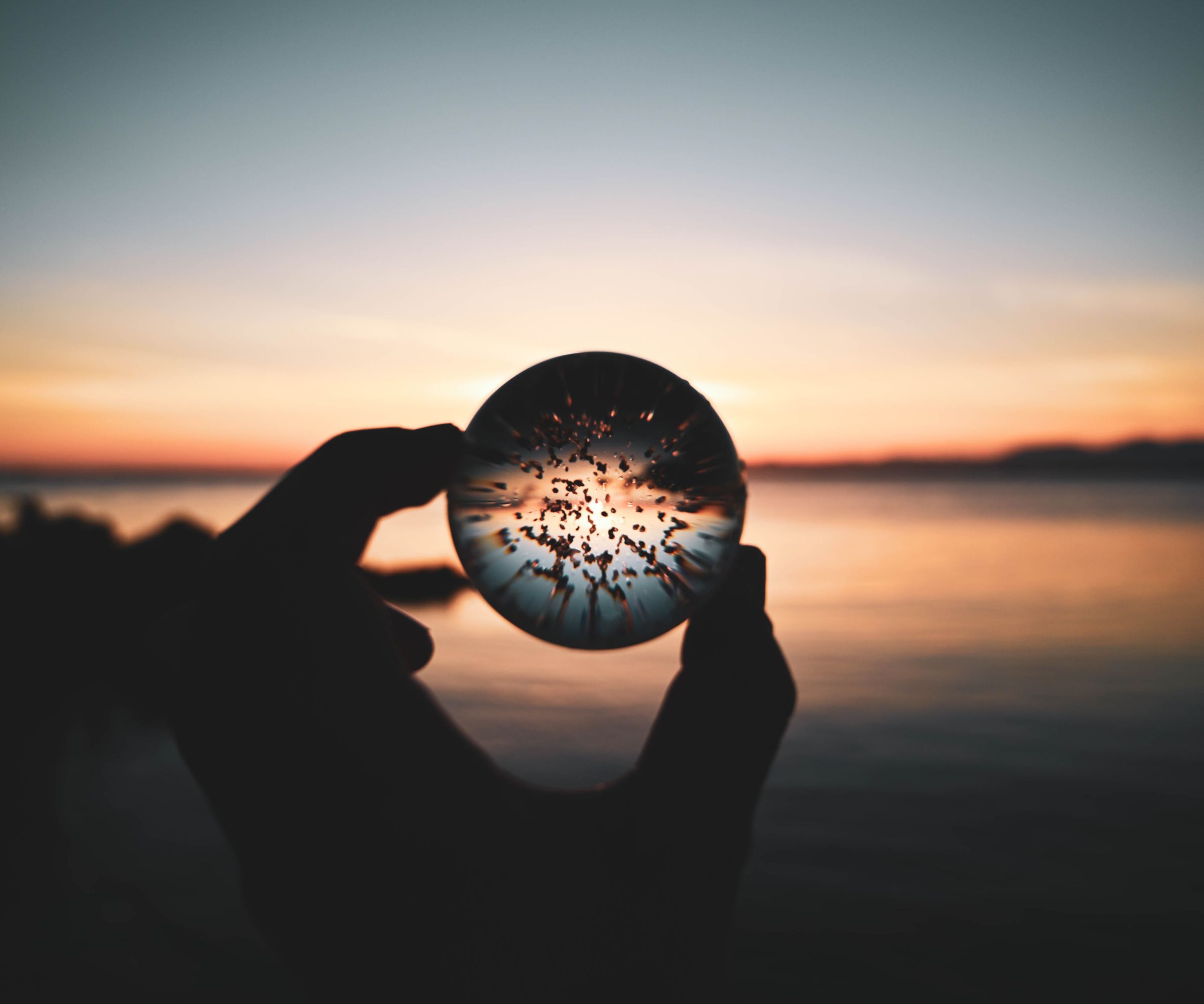 Silhouette holding glass sphere at sunset by water