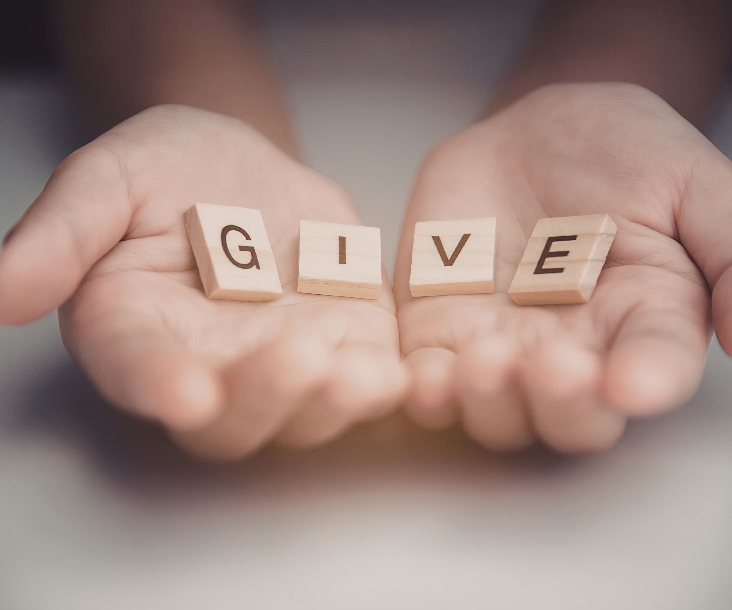 Hands holding wooden blocks spelling GIVE