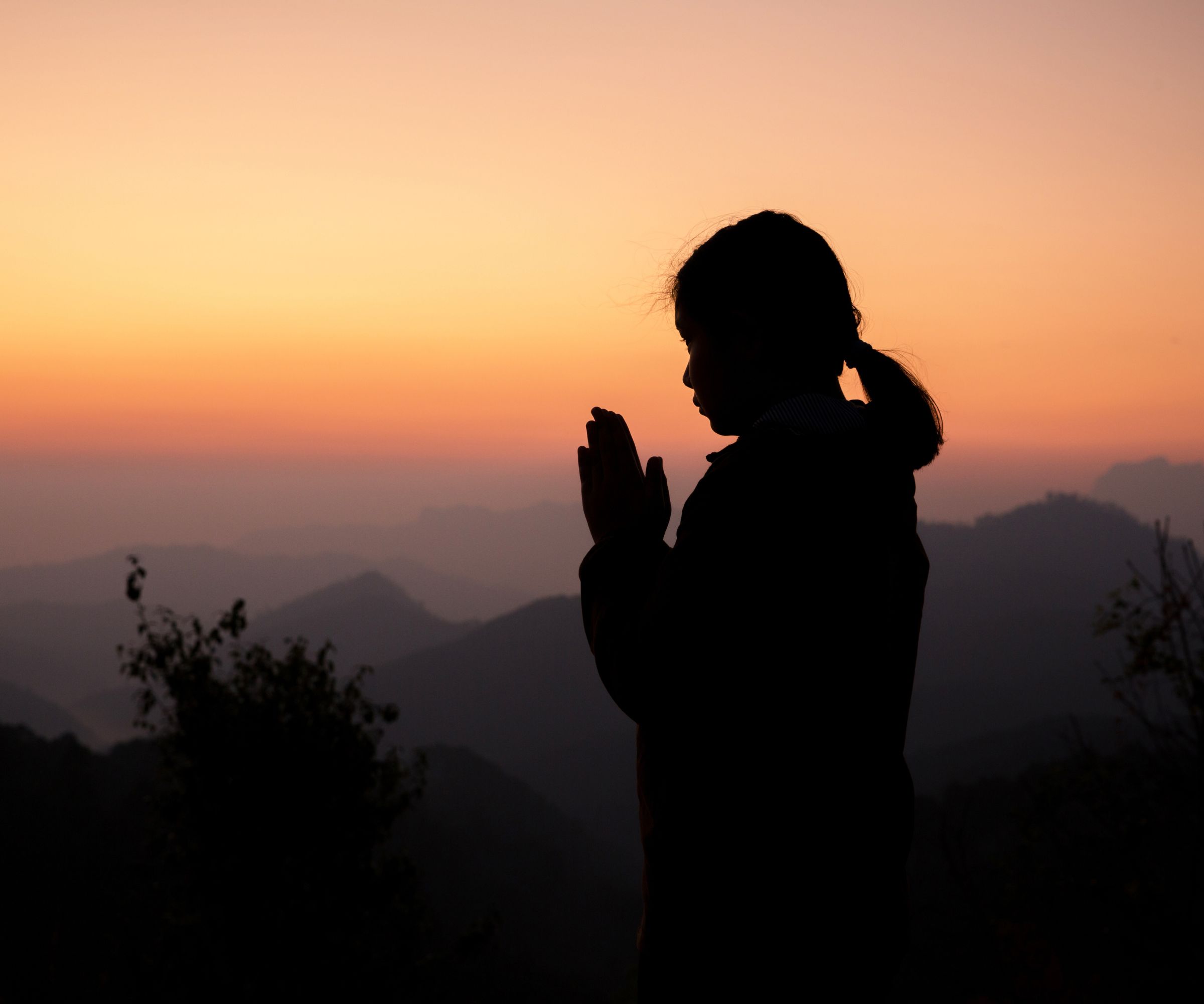 Silhouette of girl praying at sunset mountains